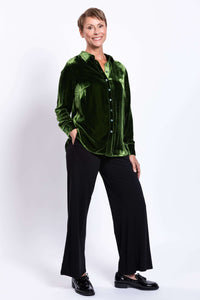 Model smiling in green silk velvet blouse with one hand in pocket