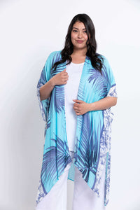 Model in turquoise palm leaf kimono wrap holding front edges, against white background