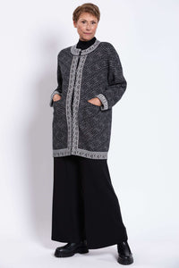 Model with hands in front pockets, wearing black and white geometric pattern cardigan