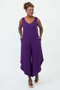Model with hands in pockets, wearing a purple sleeveless jumpsuit