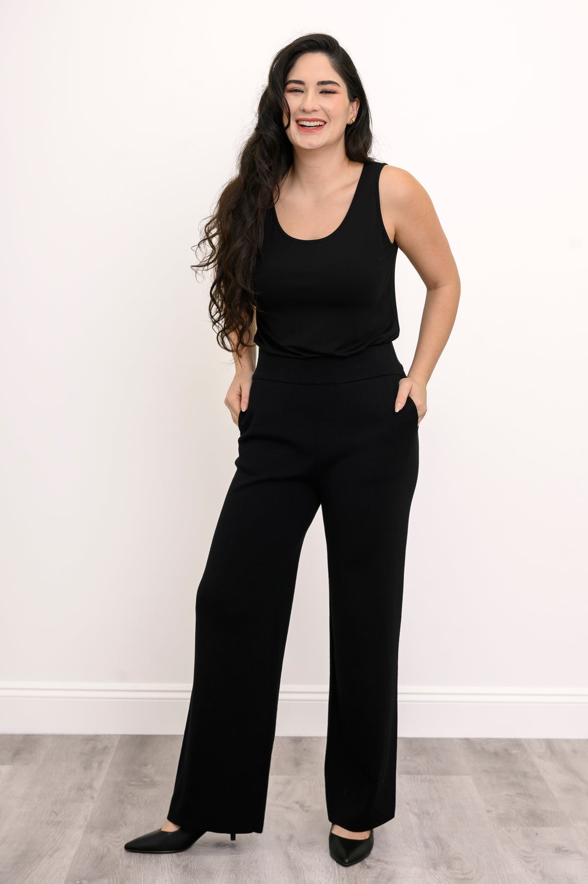 Full-length front view of a woman modeling a long, straight-cut black French terry tank top with black pants.