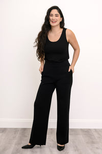 Full-length front view of a woman modeling a long, straight-cut black French terry tank top with black pants.