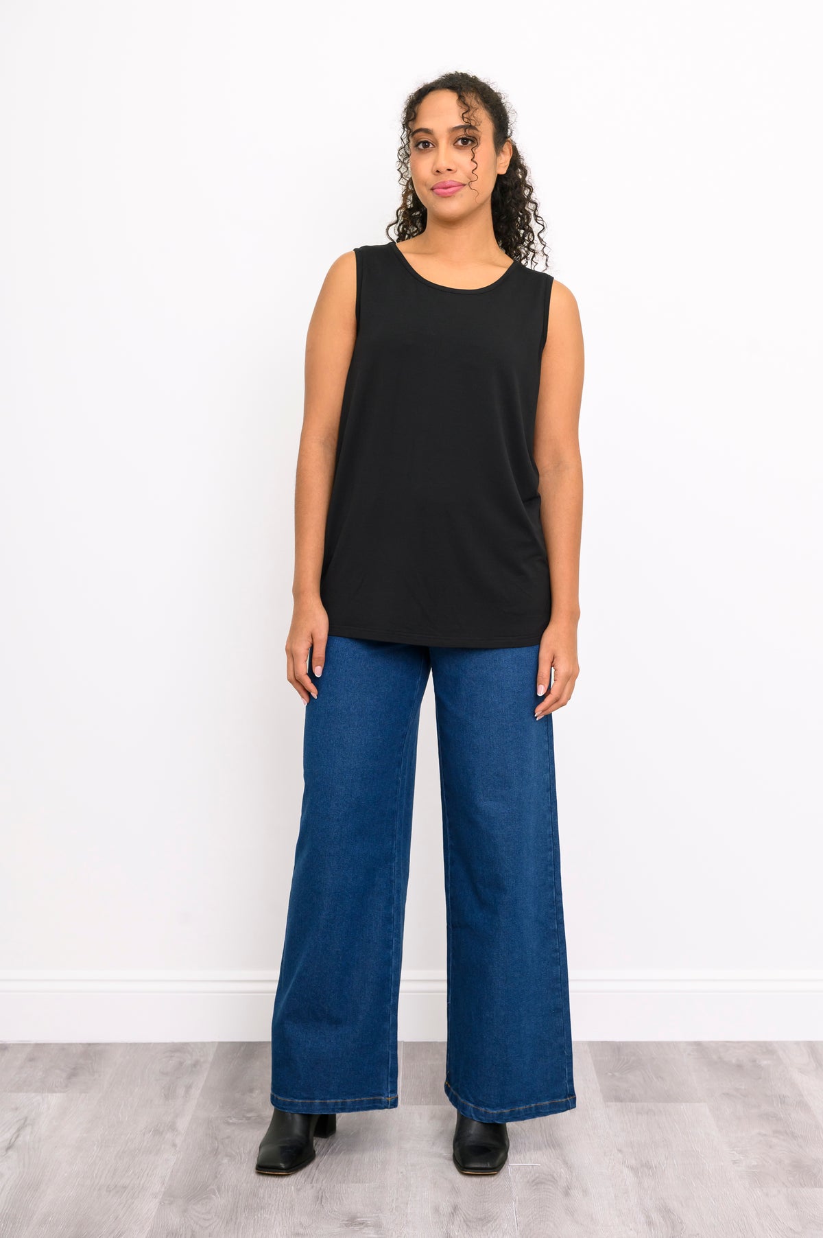 Woman wearing a casual long black bamboo layering tank top paired with dark denim jeans