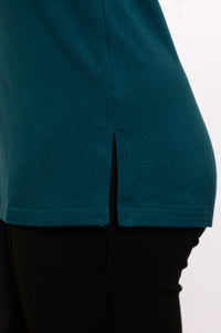 Detailed side shot of a loose-fit teal sleeveless top showcasing a split hemline layered over black trousers.