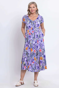 Woman smiling in a purple floral Morgan dress with hands in side pockets