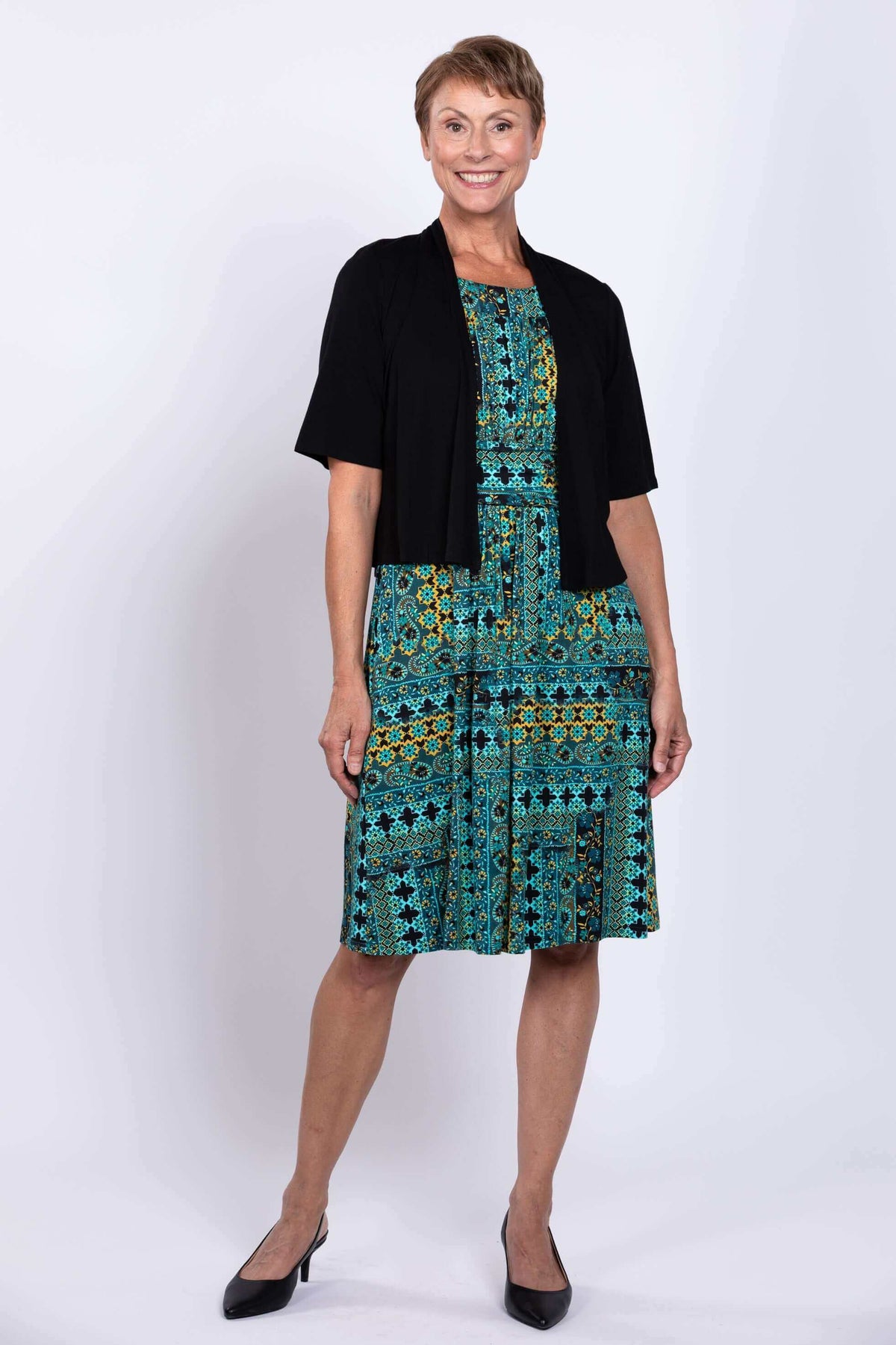 Woman in turquoise mosaic dress and black bolero, standing, front view