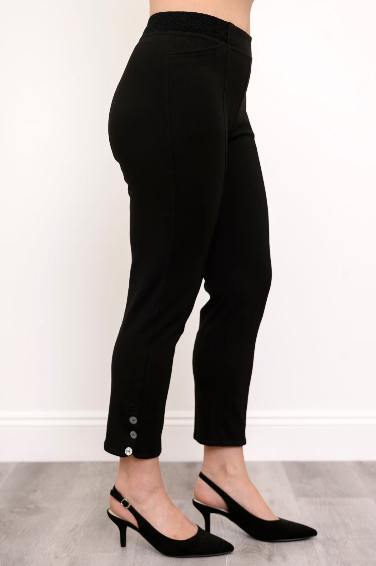 Side view of highwaisted black pants with elastic waistband and button detail at the hem