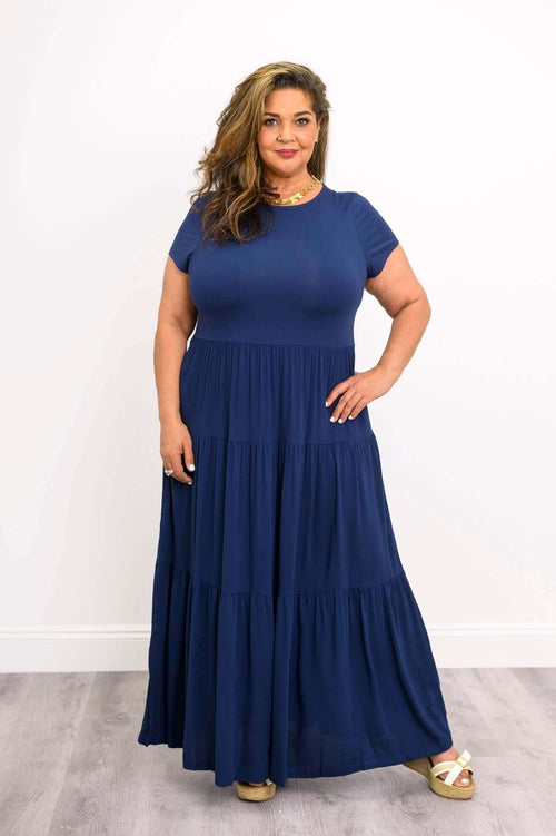 Woman wearing a navy blue short sleeve maxi dress with empire waist and flared skirt