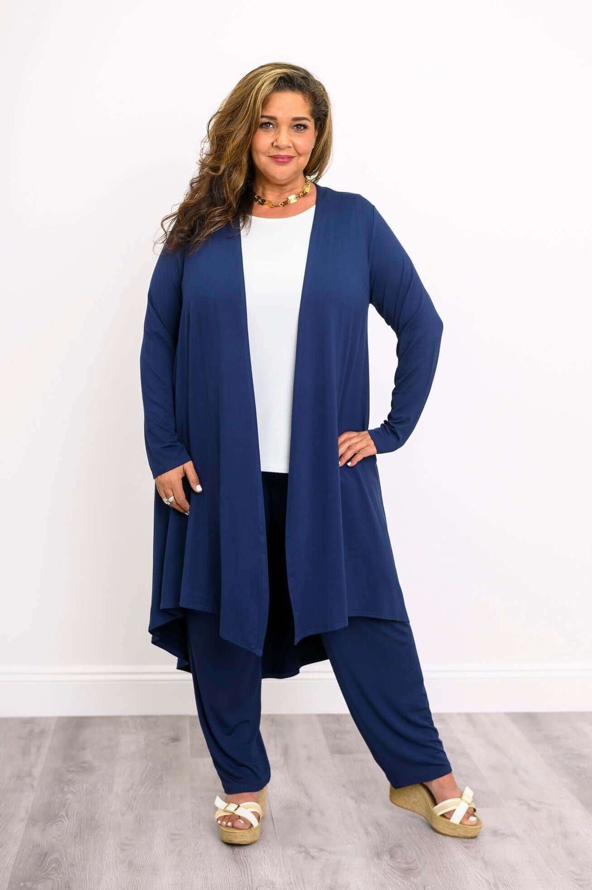 Woman with curly hair in navy duster cardigan, white top, navy pants, and wedge sandals