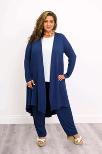Woman with curly hair in navy duster cardigan, white top, navy pants, and wedge sandals