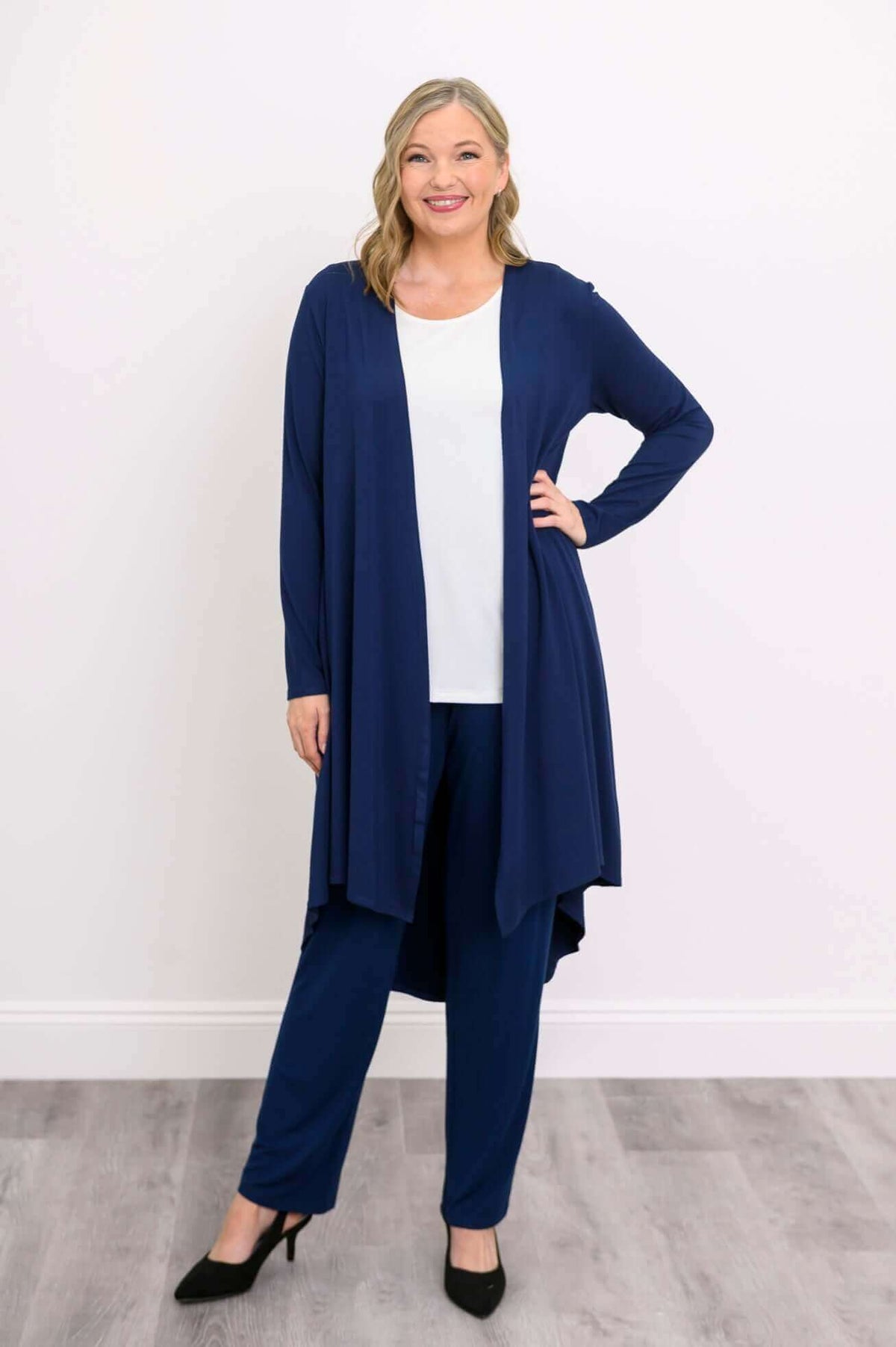 Woman smiling in a navy high-low duster cardigan, hand on hip, wearing black heels