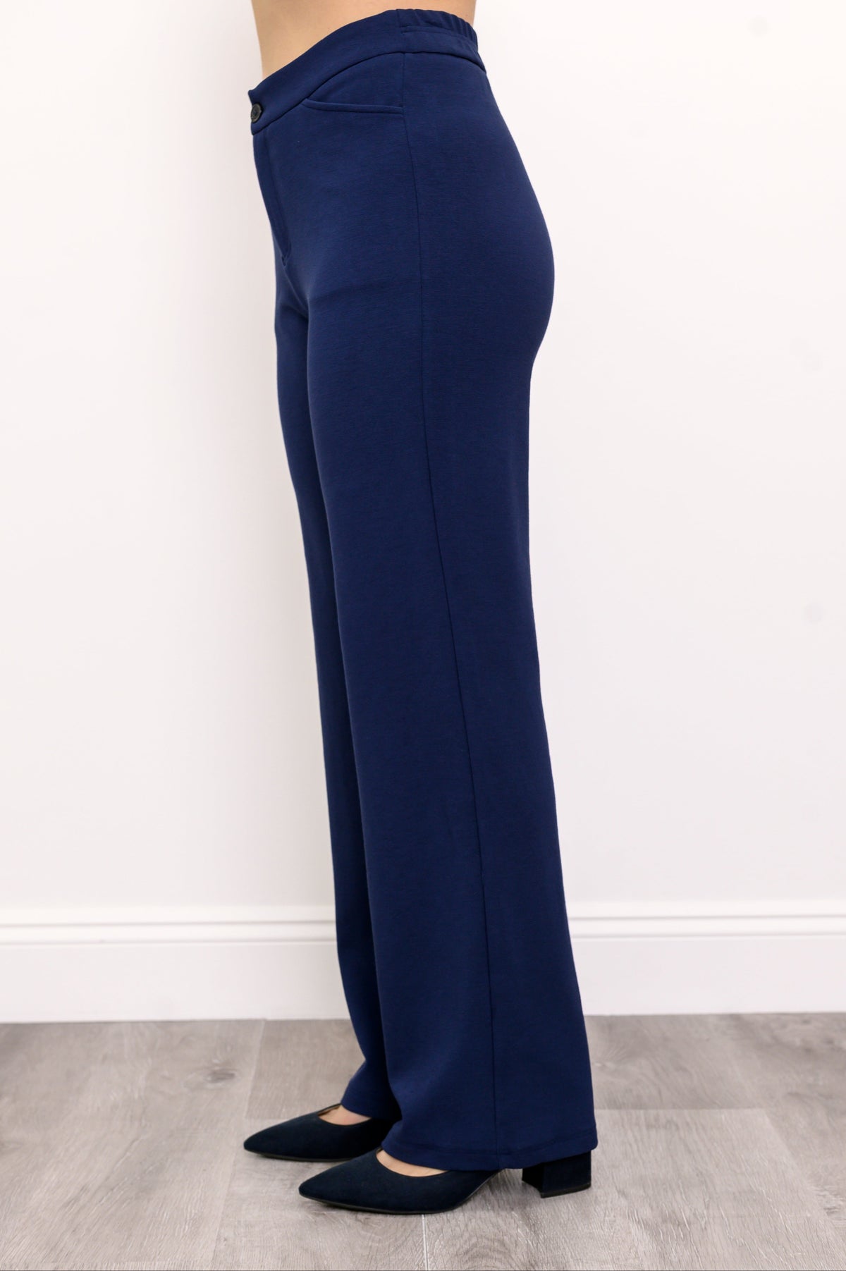 Woman wearing navy blue pants with pockets and navy blue shoes on a white background, side view