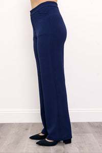 Woman wearing navy blue pants with pockets and navy blue shoes on a white background, side view