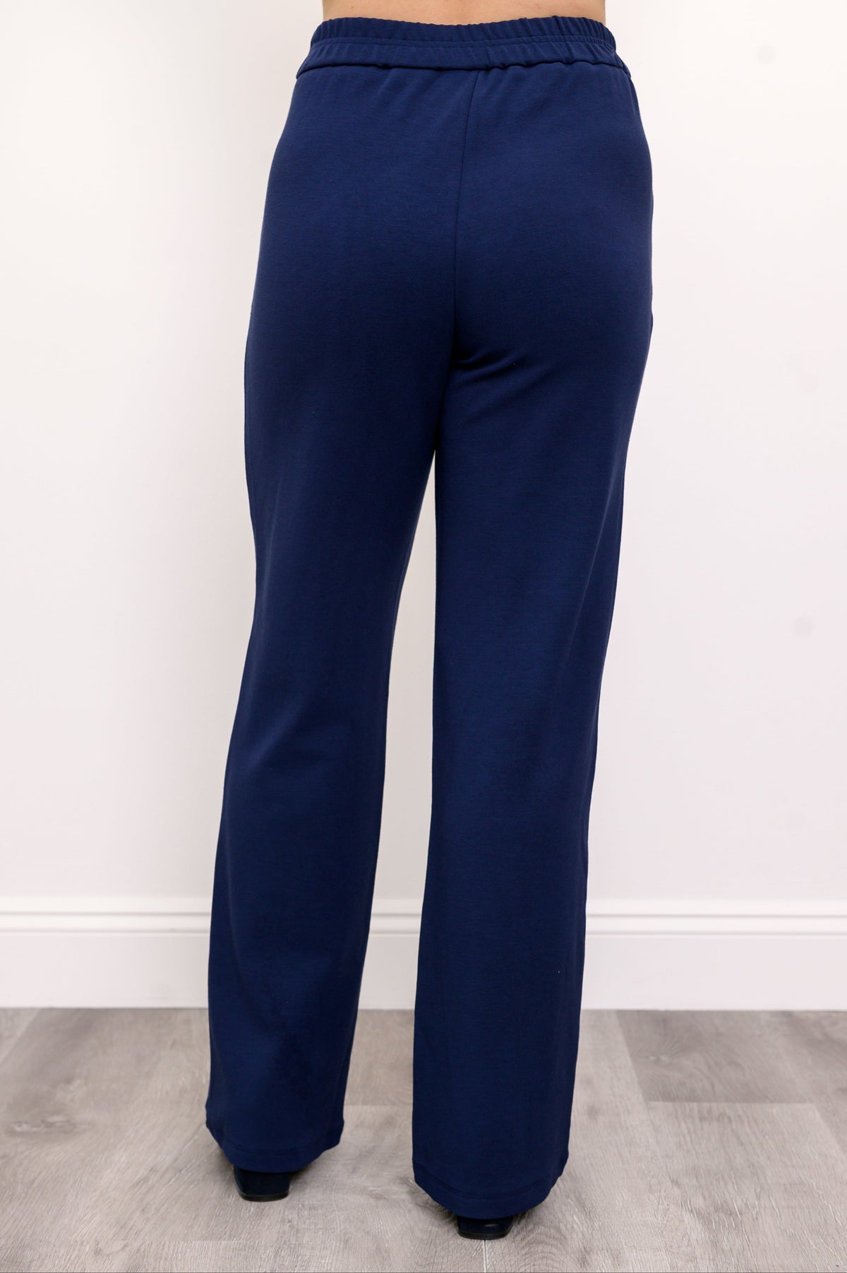 Woman wearing navy blue elasticated pants and navy blue shoes on a white background, back view