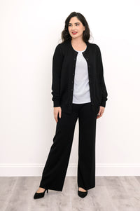 Woman modeling a hip length black button down crewneck cardigan with tailored black pants.