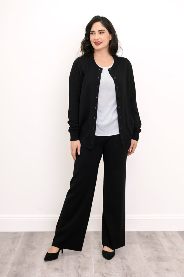 Woman modeling a hip length black button down crewneck cardigan with tailored black pants.
