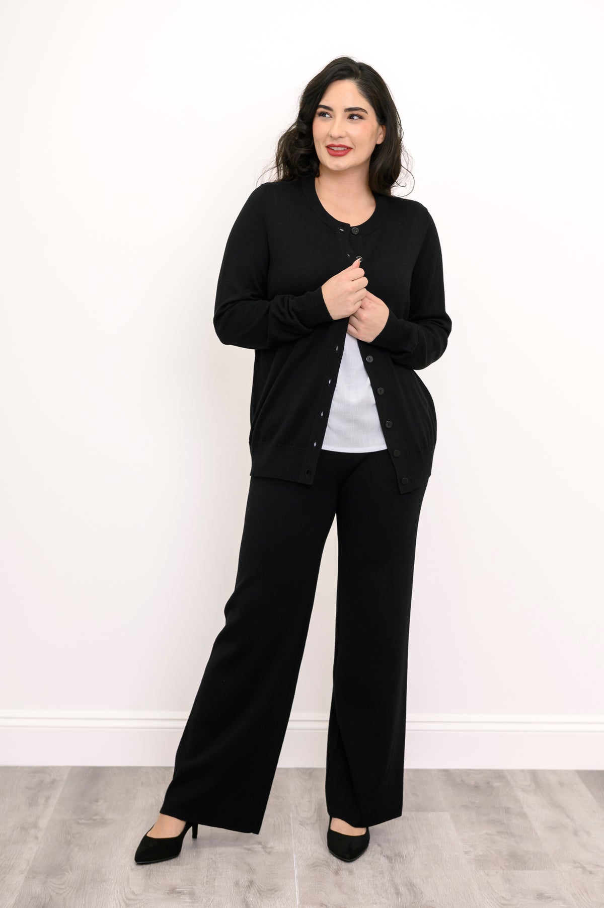 Front view of a woman wearing a black crewneck button up cardigan styled over a white t-shirt.