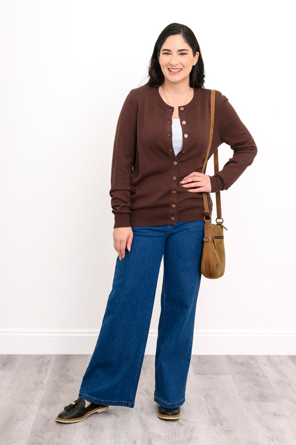 Full length view of a woman wearing a chocolate brown cotton viscose cardigan sweater and denim jeans.