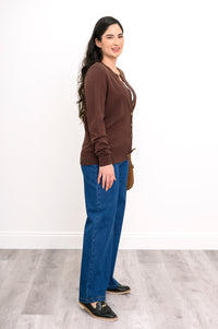 Side profile view of a woman wearing a chocolate brown long sleeve cotton knit cardigan with dark denim.