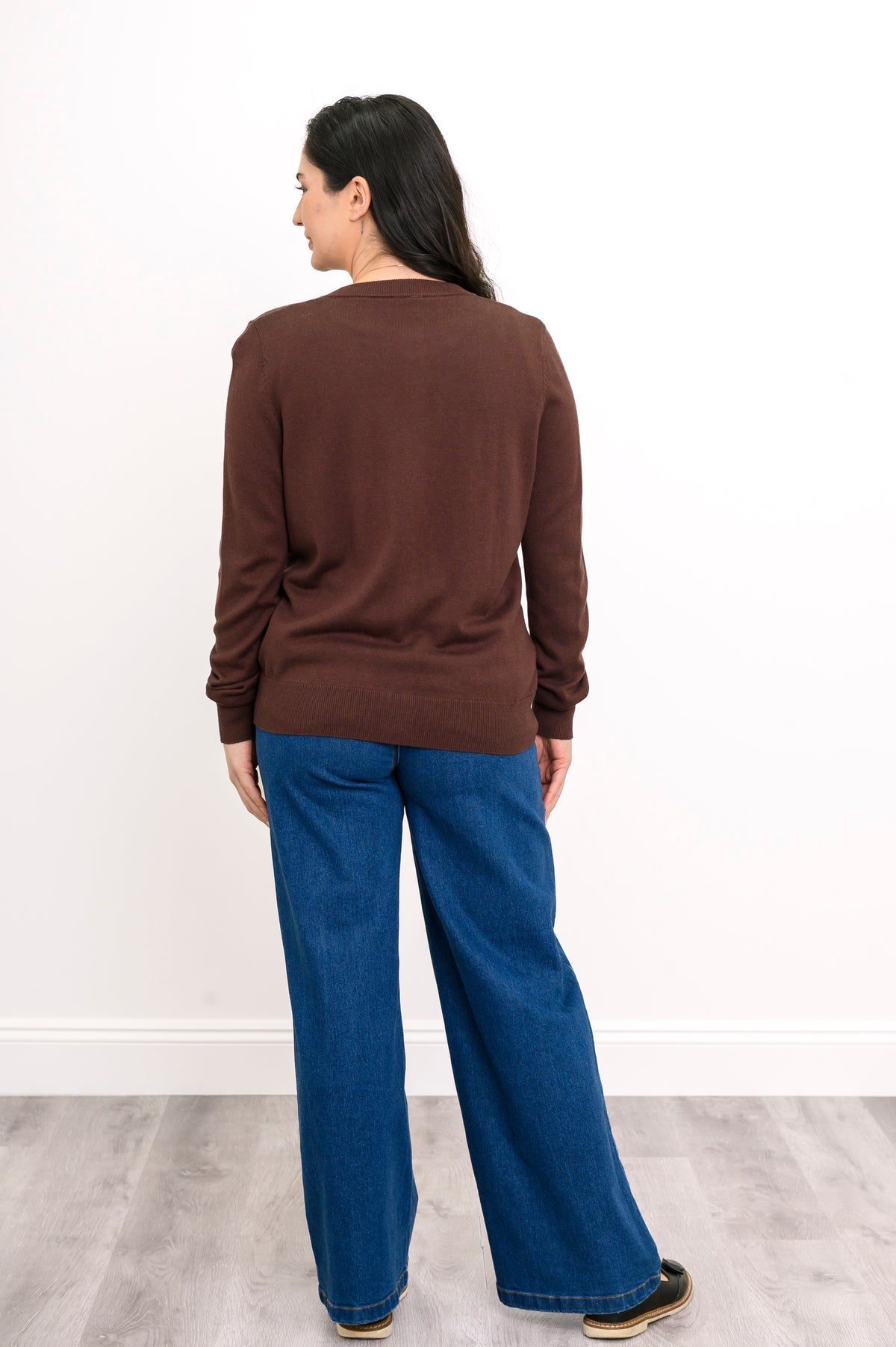 Back view of a woman wearing a hip length chocolate brown cotton viscose knit cardigan in studio.