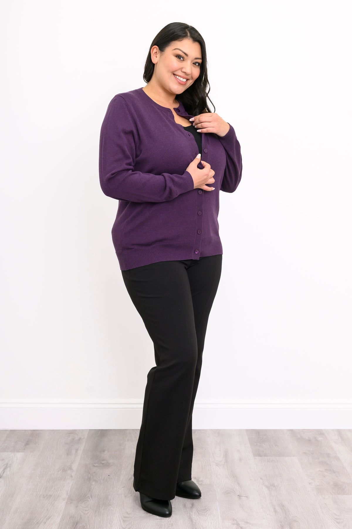 Full length view of a woman wearing an amethyst purple cotton viscose cardigan sweater and black pants.