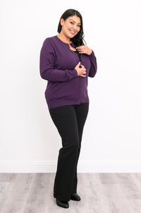 Full length view of a woman wearing an amethyst purple cotton viscose cardigan sweater and black pants.
