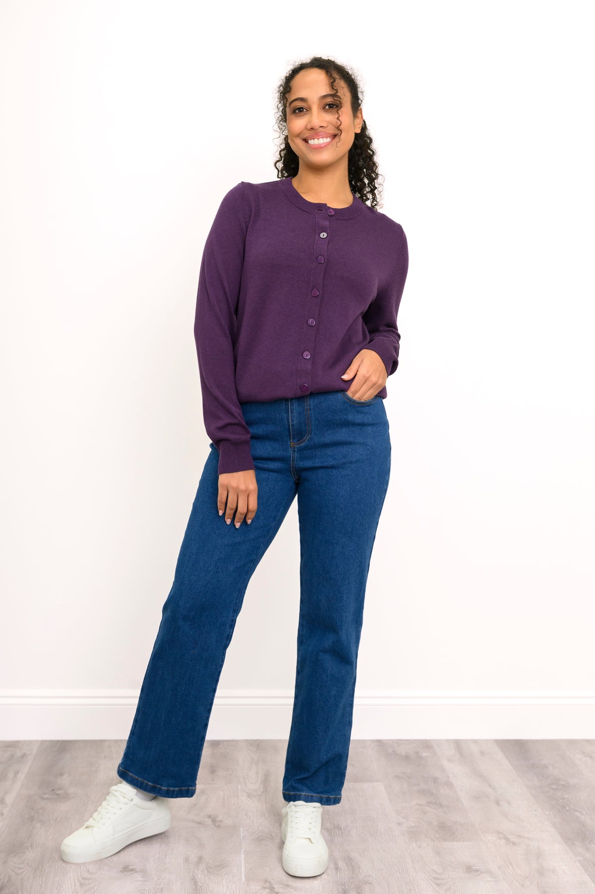 Front view of a woman wearing a purple crewneck button up cardigan styled with dark denim pants.
