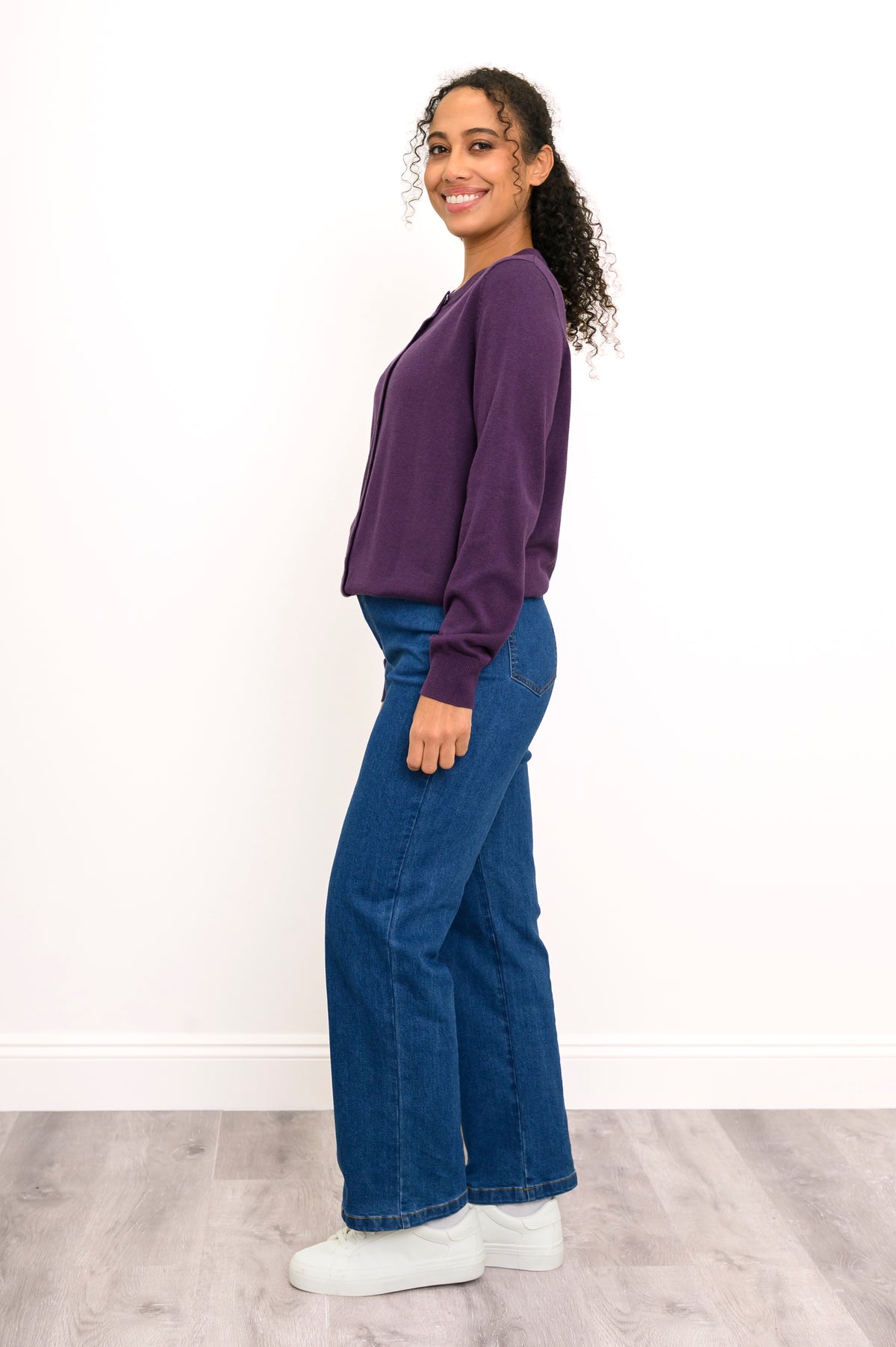 Woman modeling a casual purple buttoned knit cardigan sweater paired with dark blue denim pants.