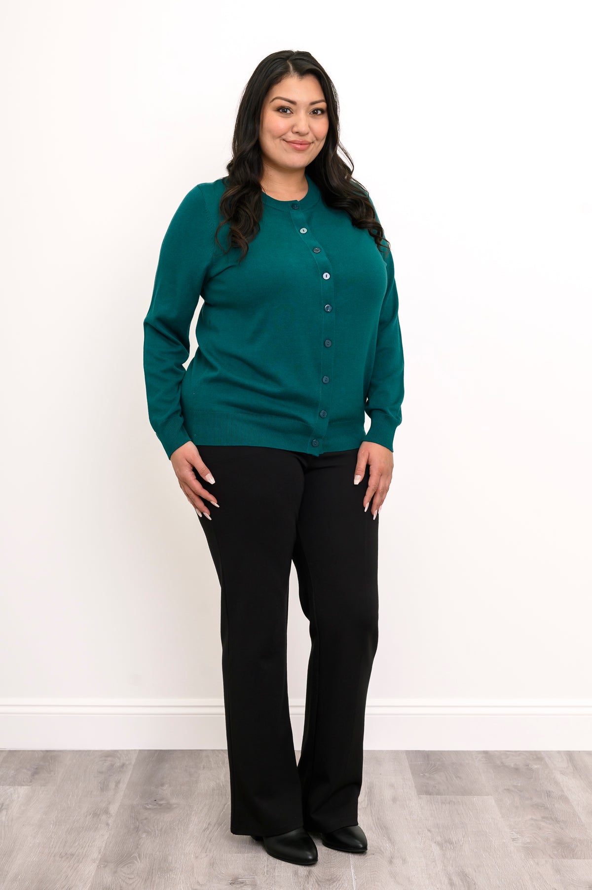 Full length view of a woman wearing a teal green cotton viscose cardigan sweater and black pants.