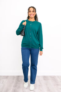 Full length shot of a woman in a teal button down knit top with a black crossbody purse and jeans.