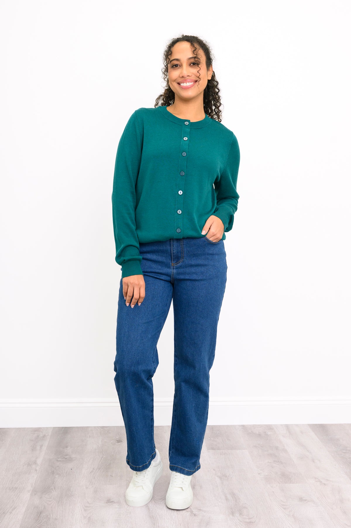 Woman modeling a casual emerald green buttoned knit sweater paired with denim pants on white.