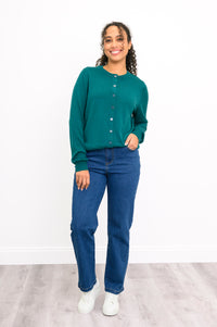 Woman modeling a casual emerald green buttoned knit sweater paired with denim pants on white.