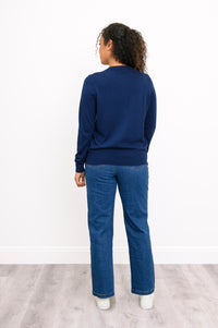 Back view of a woman wearing a hip length navy blue cotton viscose knit cardigan and denim jeans.