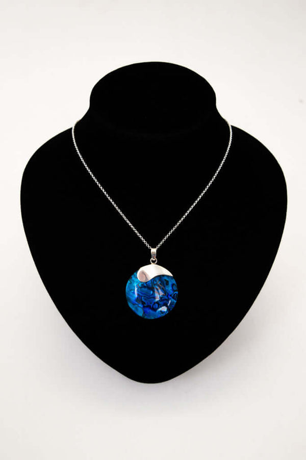 Oceanic blue shell and silver pendant necklace displayed on a black necklace bust