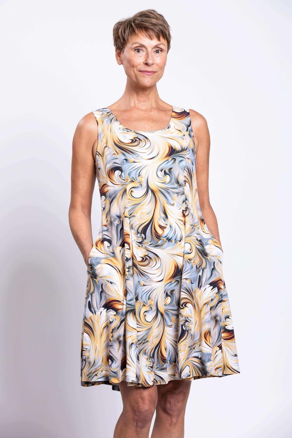 Older woman in sleeveless swirl print dress standing with hands in pockets