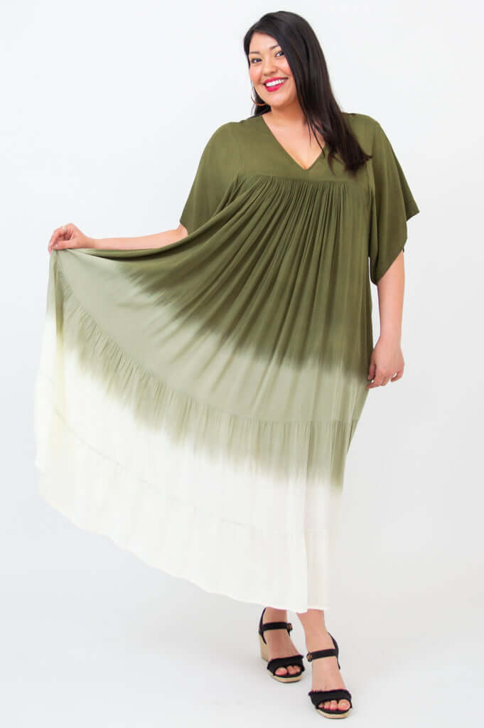 Woman displaying the full width of an olive ombre maxi dress by holding out the skirt