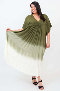 Woman displaying the full width of an olive ombre maxi dress by holding out the skirt
