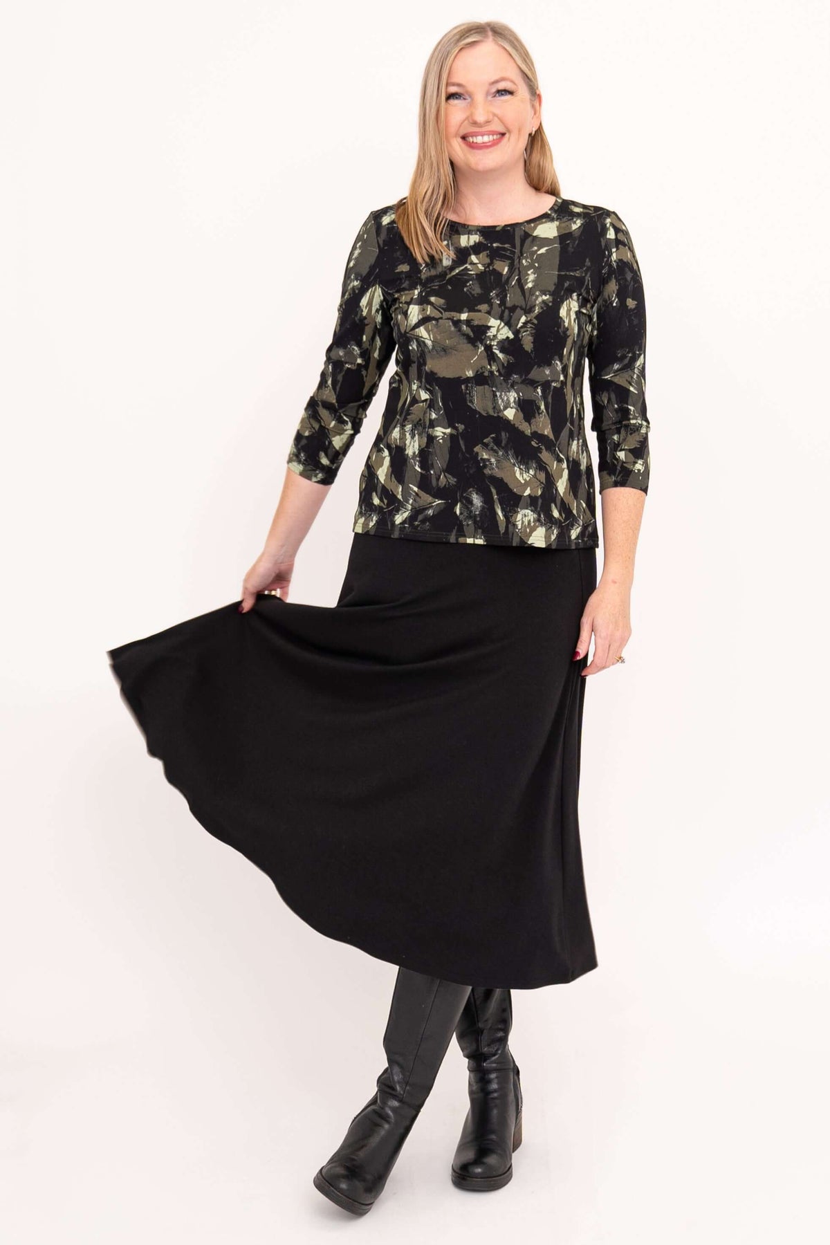 Woman playfully holding skirt while wearing olive print tee and black skirt