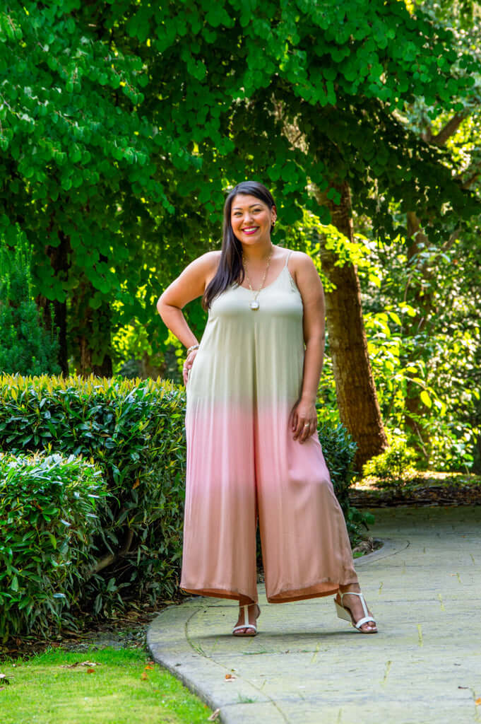 Model posing outdoors in a beige to blush ombre jumpsuit with adjustable straps