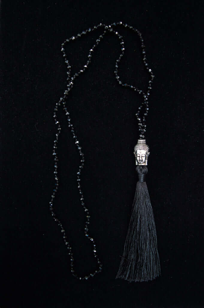 Black onyx beaded necklace with a silver Buddha head and long black tassel on a black background