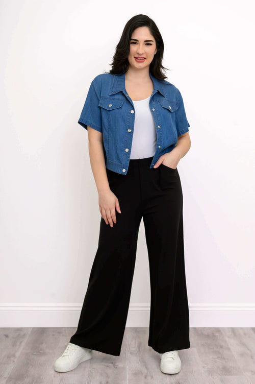Model with unbuttoned denim jacket over white top and black wide-leg pants