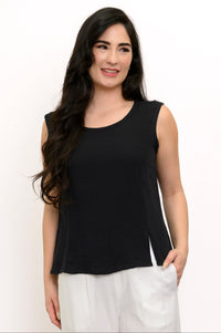Woman wearing a black sleeveless top and white pants against a white background, front view