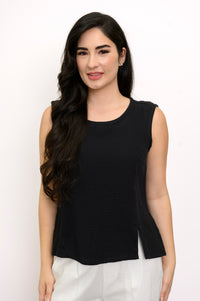 Woman wearing a black sleeveless top and white pants against a white background, front view
