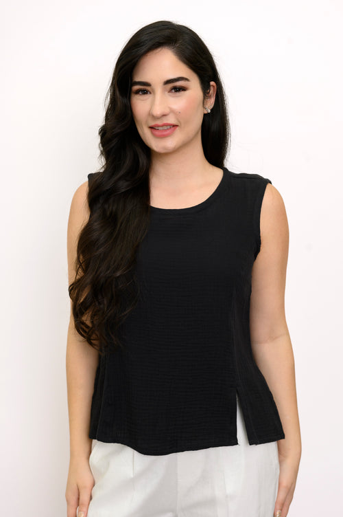 Woman wearing a black sleeveless top and white pants against a white background, front view