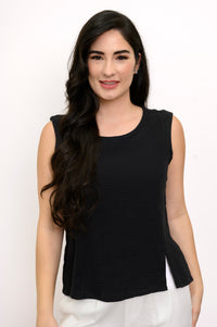 Woman wearing a black sleeveless top and white pants against a white background, front view