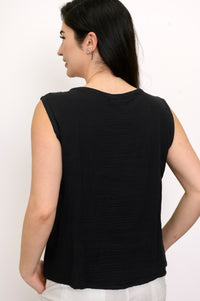 Woman wearing a black sleeveless top and white pants against a white background, back view