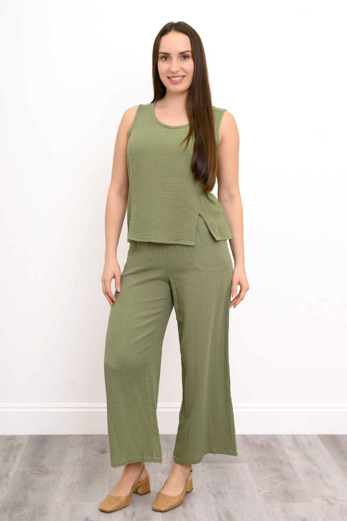 Woman wearing a green sleeveless top, wide-leg pants against, and tan shoes against a white background, front view