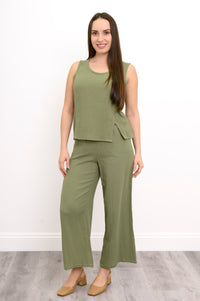 Woman wearing a green sleeveless top, wide-leg pants against, and tan shoes against a white background, front view