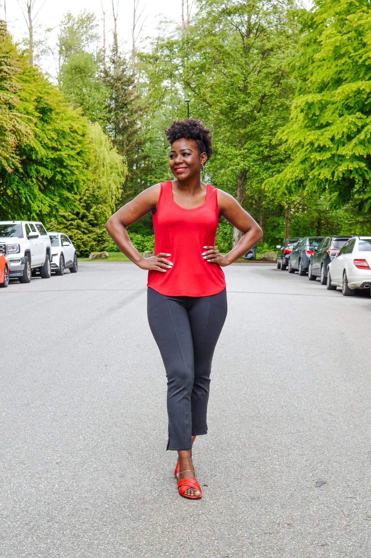 Woman outdoors wearing bright red tank top and black pants, hands on hips