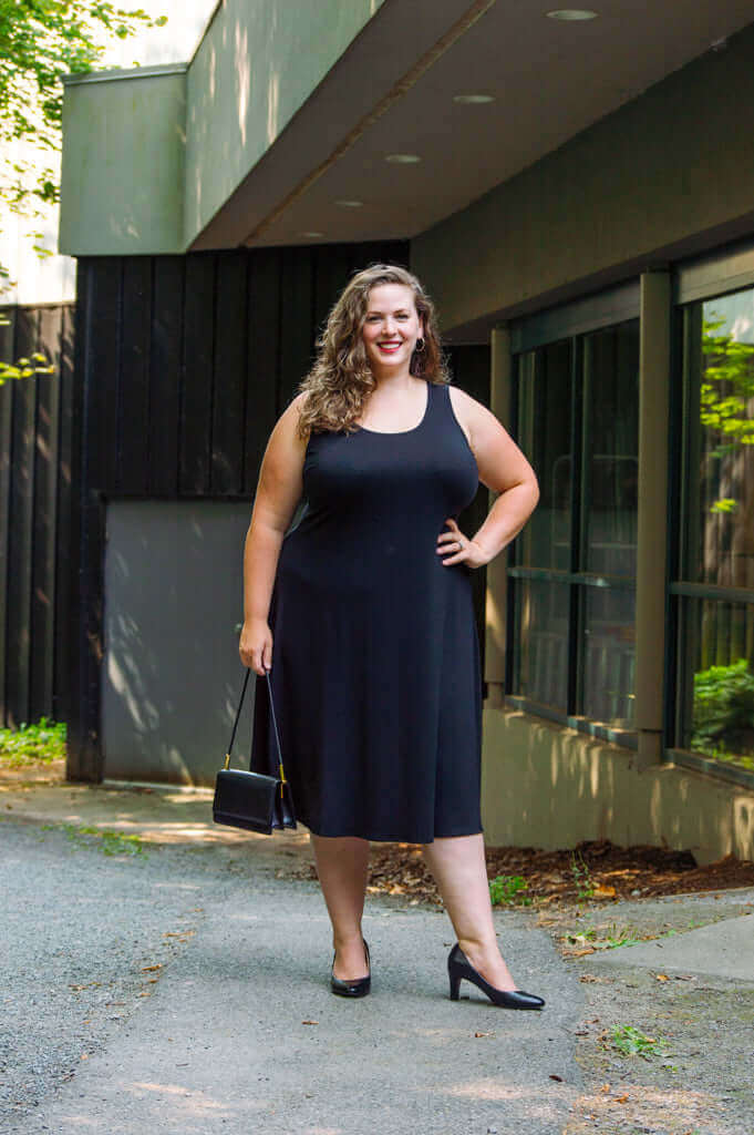 Woman outdoors in a sleeveless black dress with scoop neckline and black heels